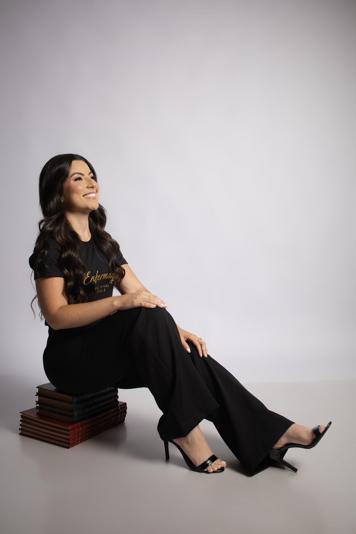 Formanda de Enfermagem sentada sobre livros