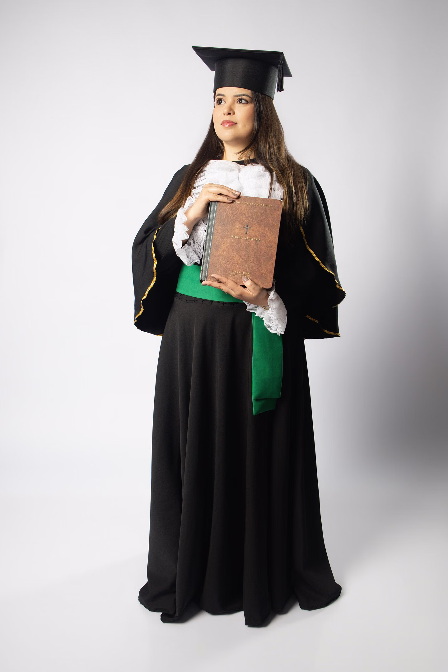 Juliana de beca verde e capelo, segurando a Bíblia no ensaio de formatura em Belo Horizonte