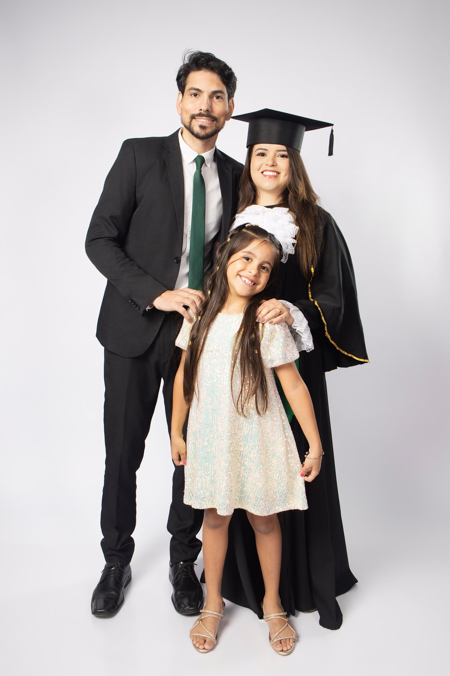 Juliana de beca ao lado de um homem e uma menina, os três sorrindo no ensaio de formatura em Belo Horizonte
