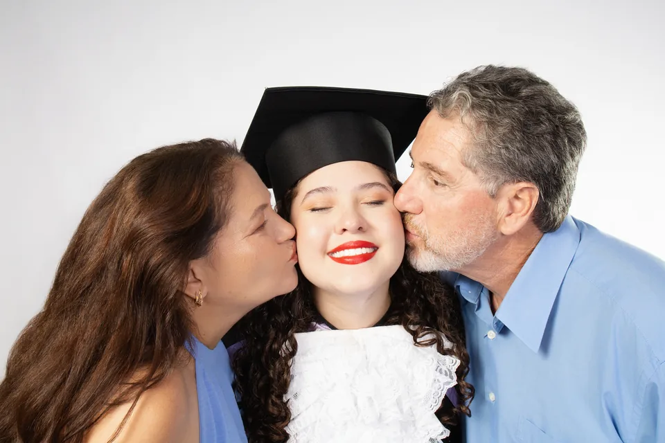 Bruna de beca recebendo um beijo de dois familiares no ensaio de formatura de Letras