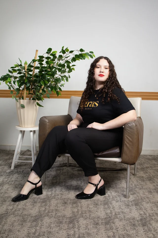 Bruna sentada na poltrona do estúdio usando a camisa personalizada de Letras.