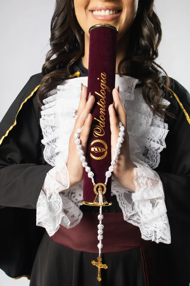 Detalhe das mãos de Bárbara com o canudo de Odontologia e o terço durante o ensaio de formatura