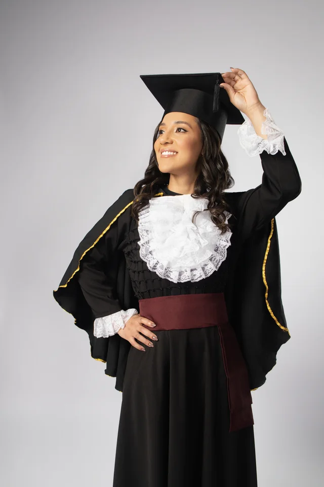 Bárbara sorrindo de beca de Odontologia, com uma das mãos no capelo, no ensaio de formatura em Belo Horizonte