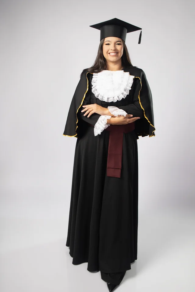 Ysabella de corpo inteiro usando beca e capelo de Odontologia no ensaio de formatura em Belo Horizonte