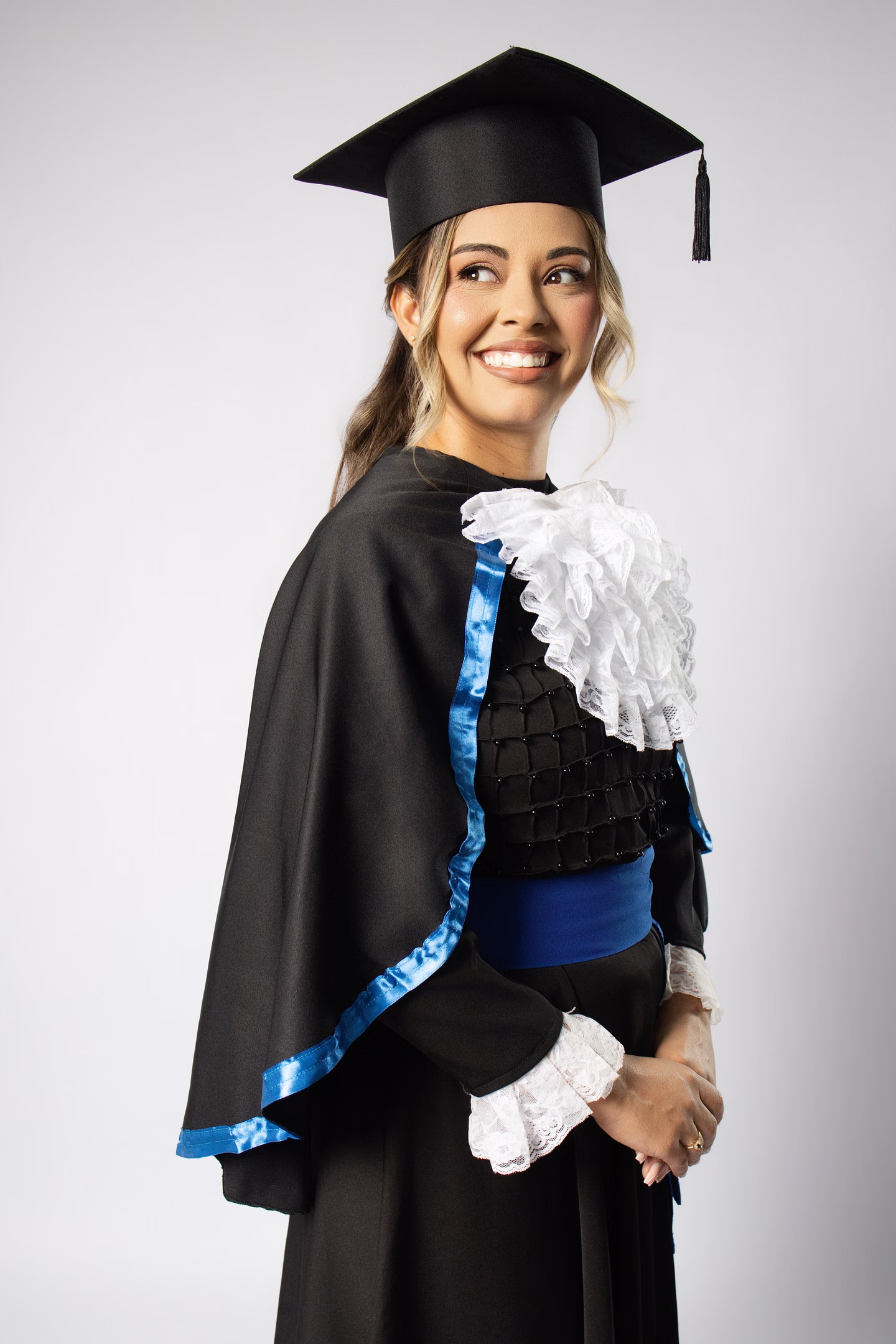 Aline com beca azul e capelo, sorrindo de lado no ensaio de formatura em Belo Horizonte