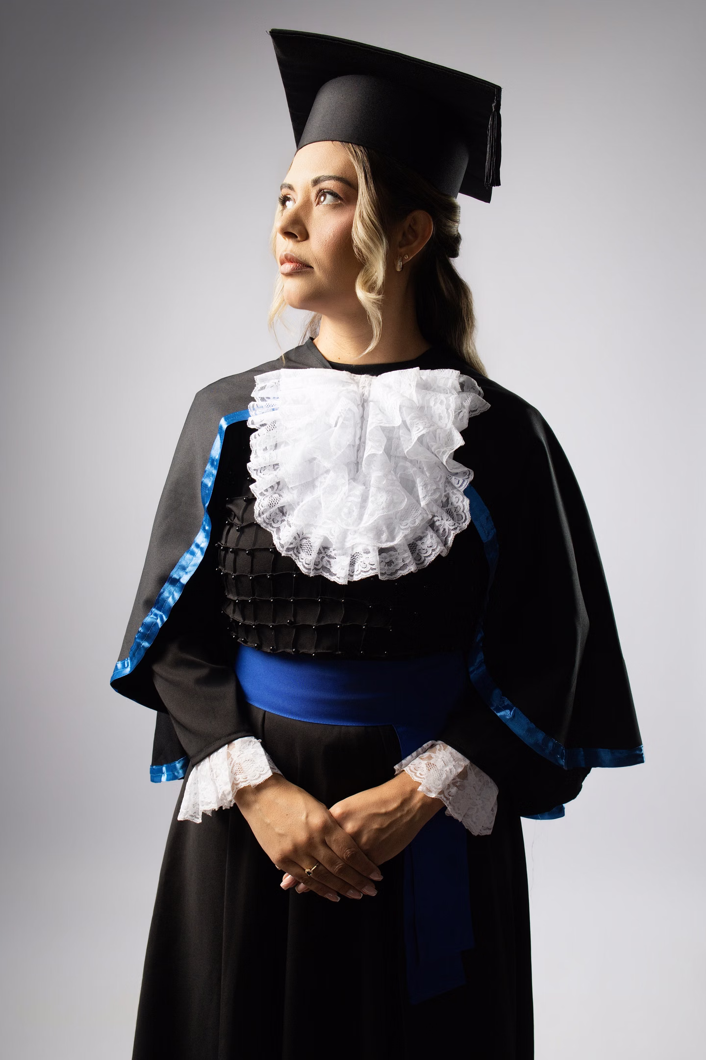 Aline sorrindo de lado com beca azul no ensaio de formatura em Belo Horizonte