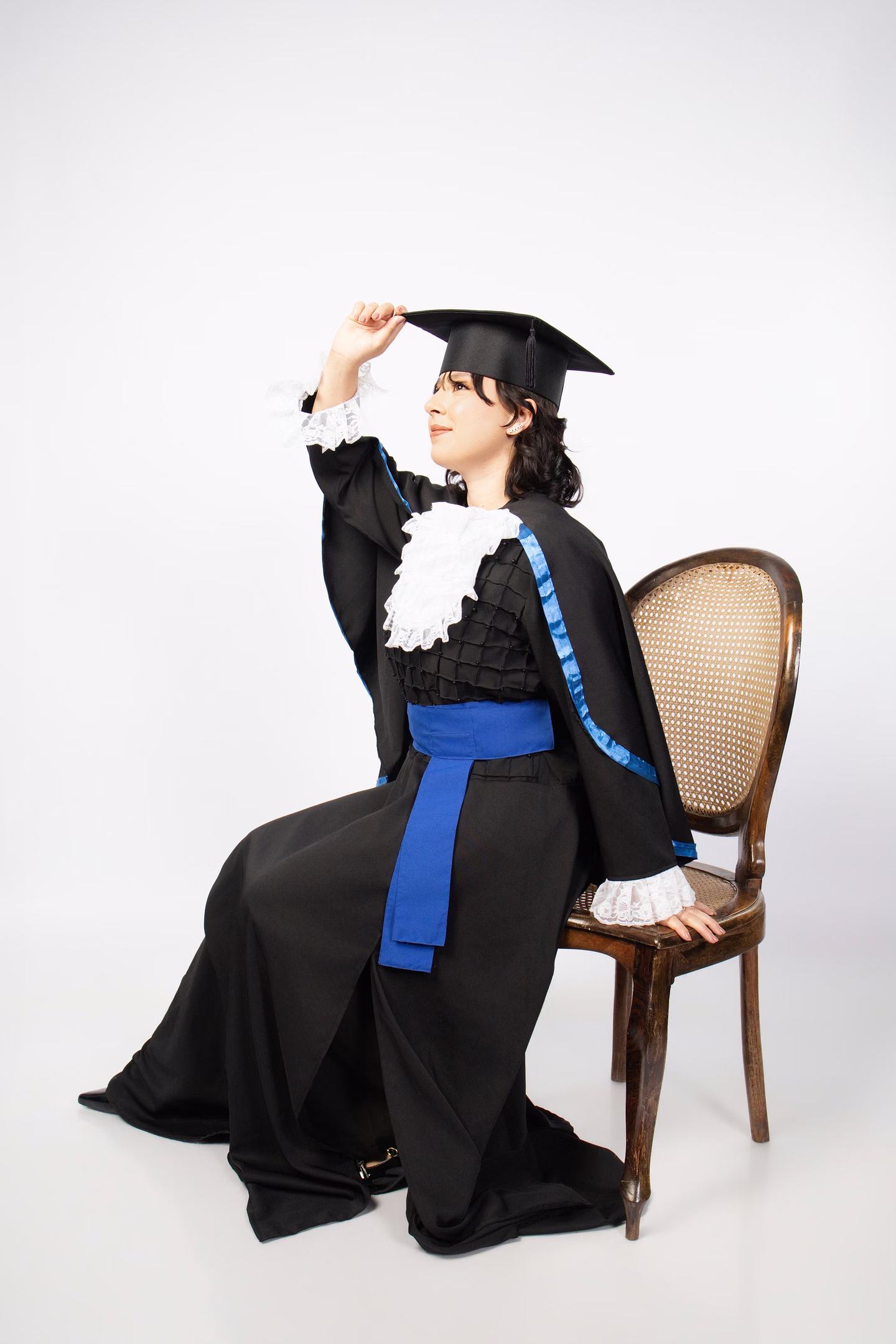Clara sentada com beca e tocando o capelo no ensaio de formatura em Belo Horizonte