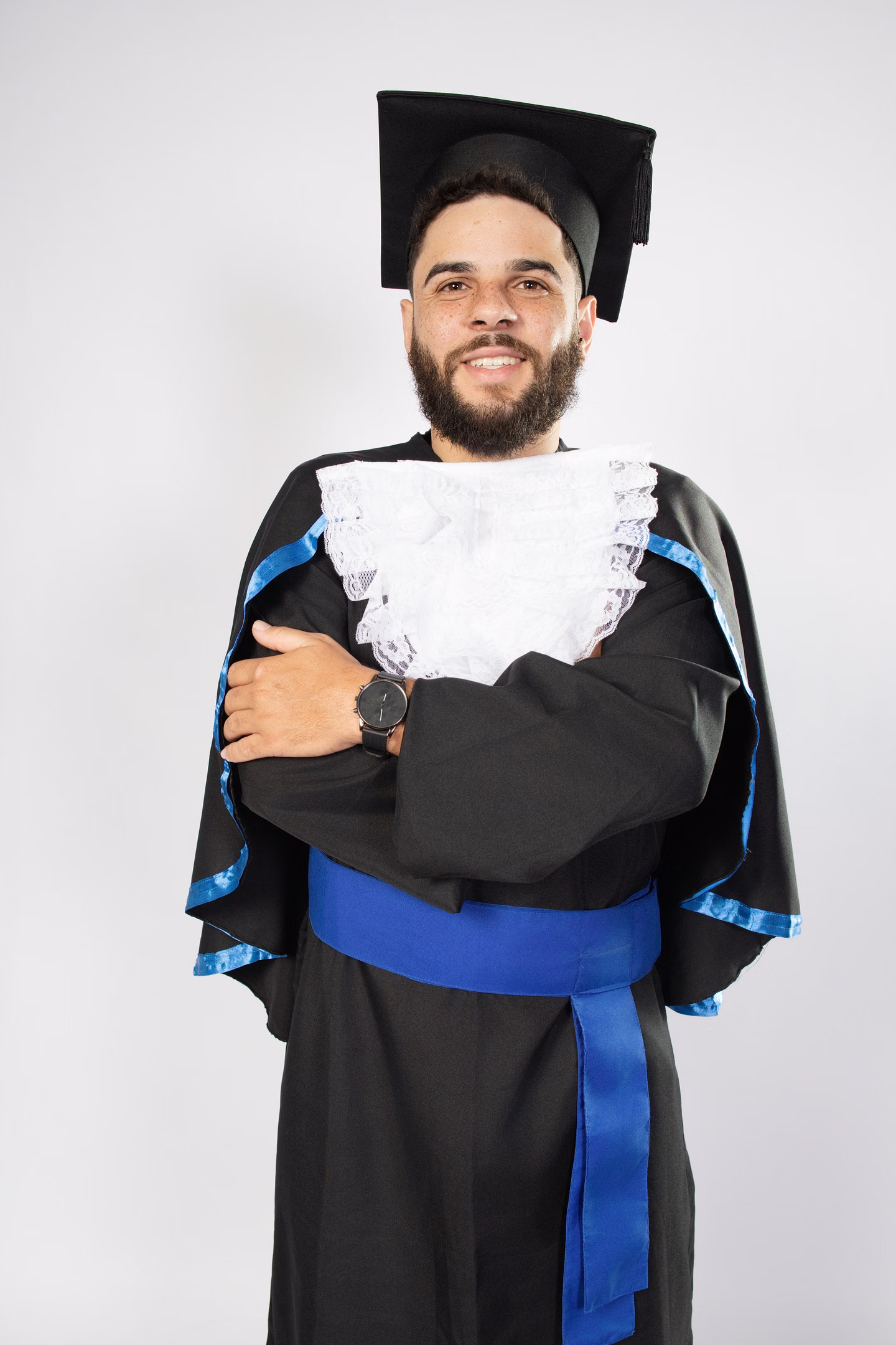 Felipe Diogo sorrindo com beca azul e braços cruzados no ensaio de formatura em Belo Horizonte