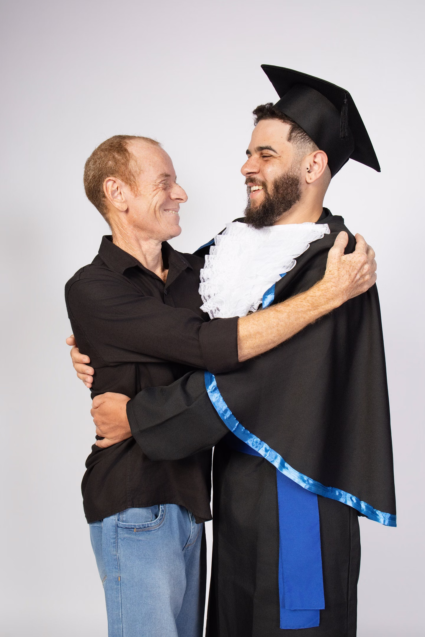 Felipe Diogo de beca abraçando um homem, os dois rindo no ensaio de formatura em Belo Horizonte