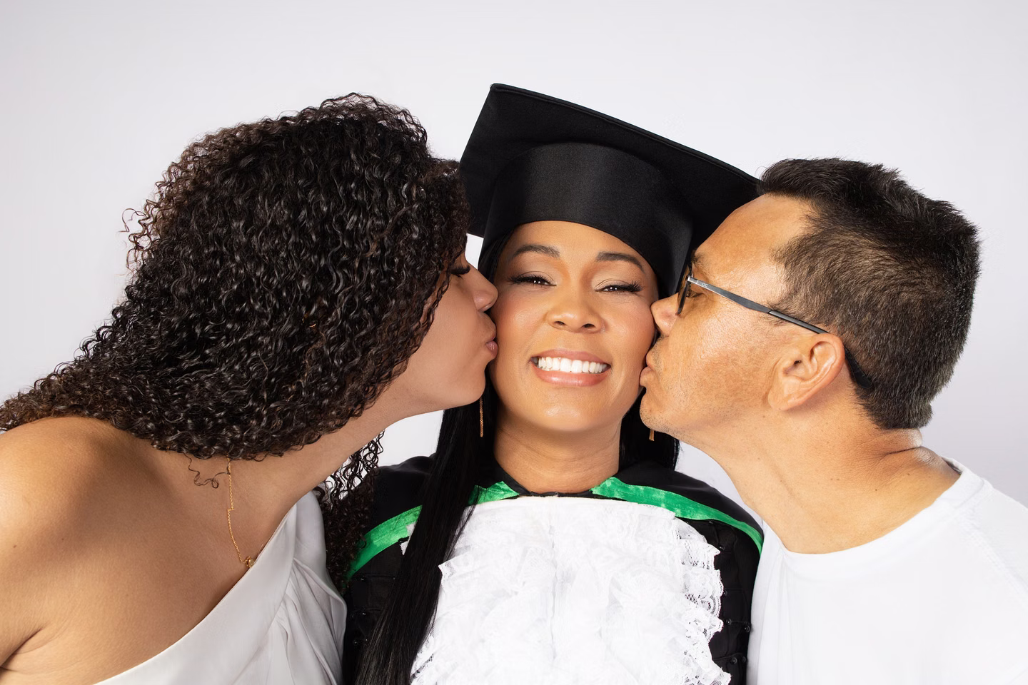 Lilian de beca recebendo dois beijos no rosto de seus acompanhantes no ensaio de formatura em Belo Horizonte