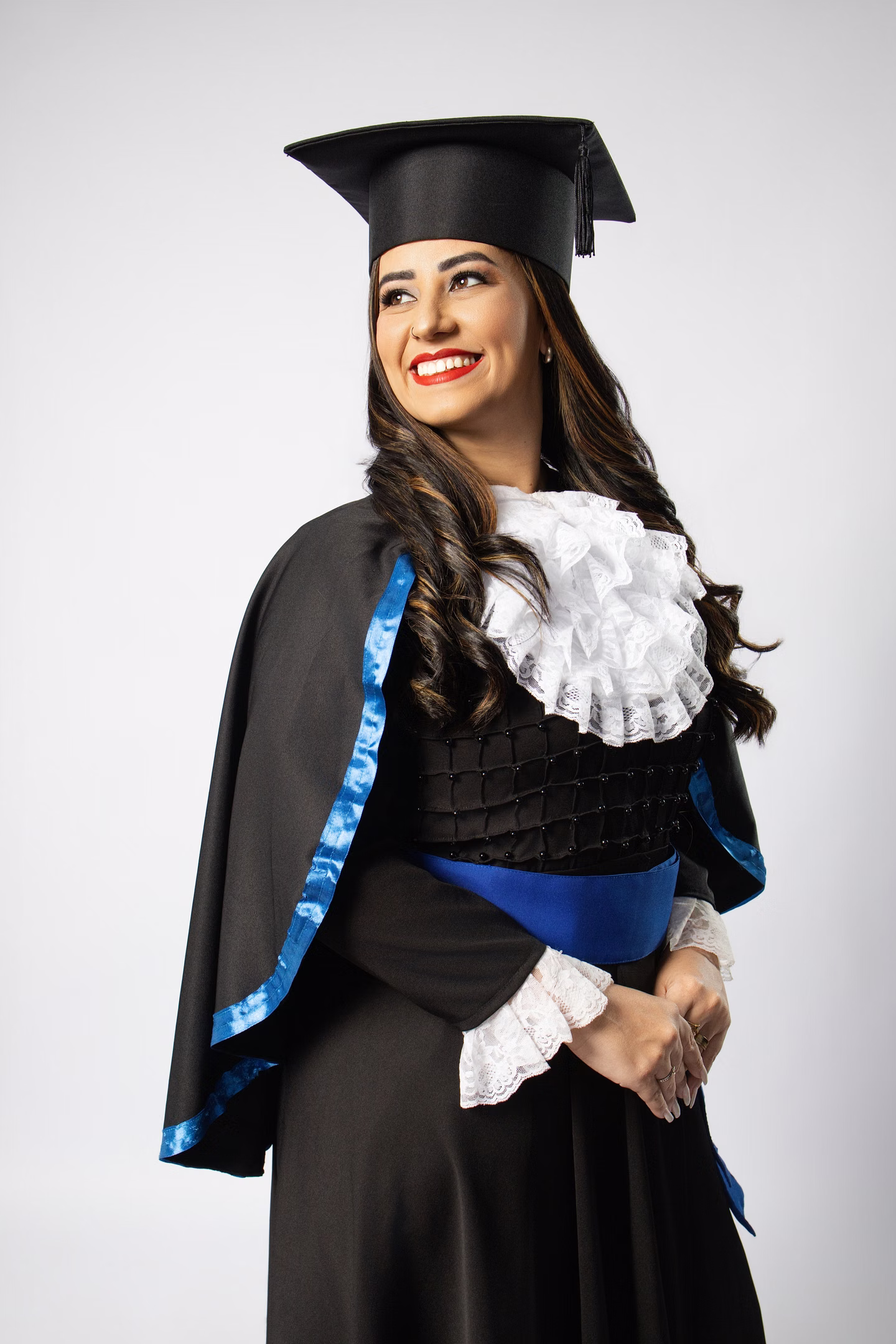 Meryen sorrindo de lado com beca azul e capelo no ensaio de formatura em Belo Horizonte