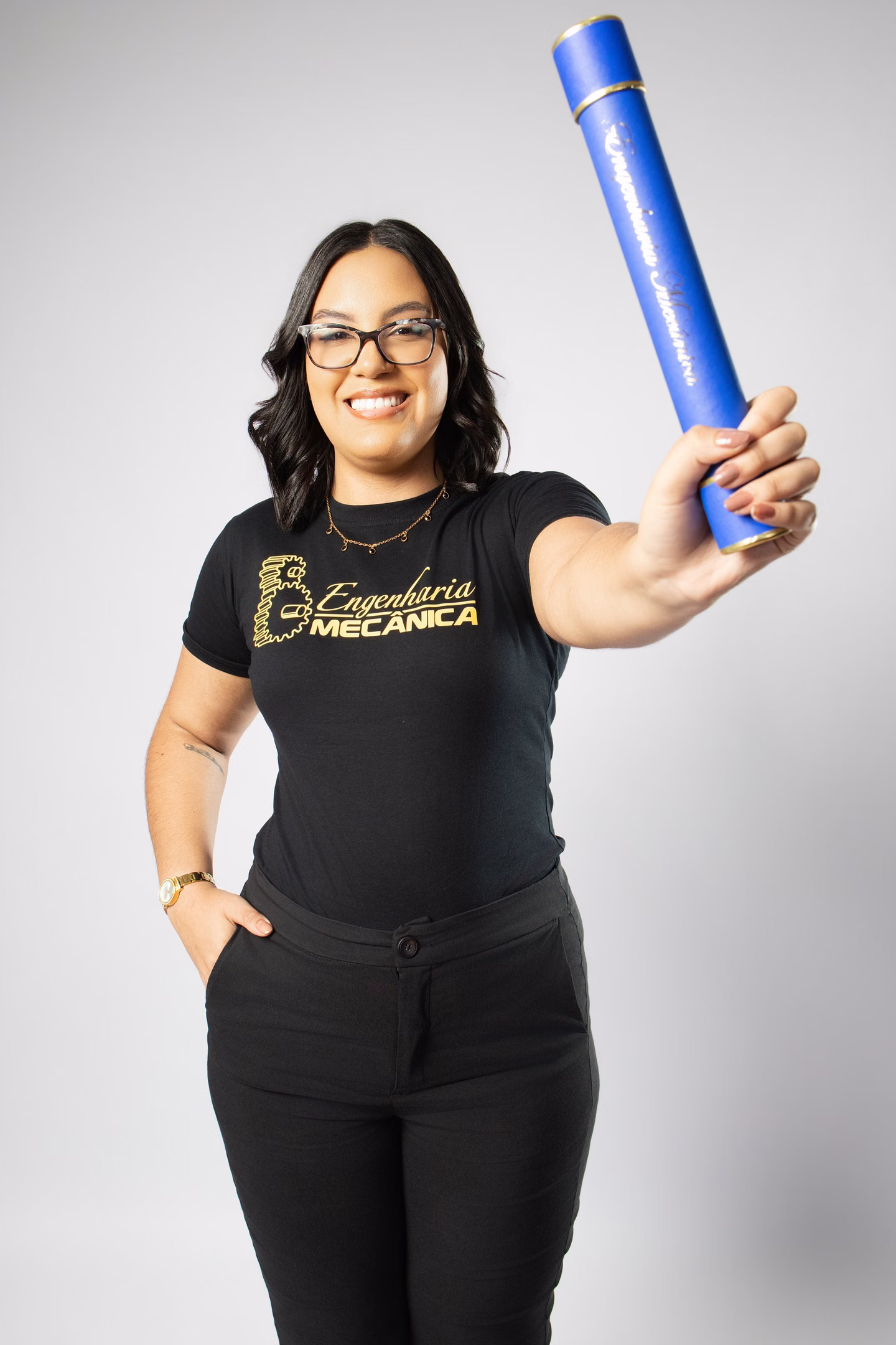 Samara com a camisa do curso e um diploma azul voltado para a câmera no ensaio de formatura em Belo Horizonte