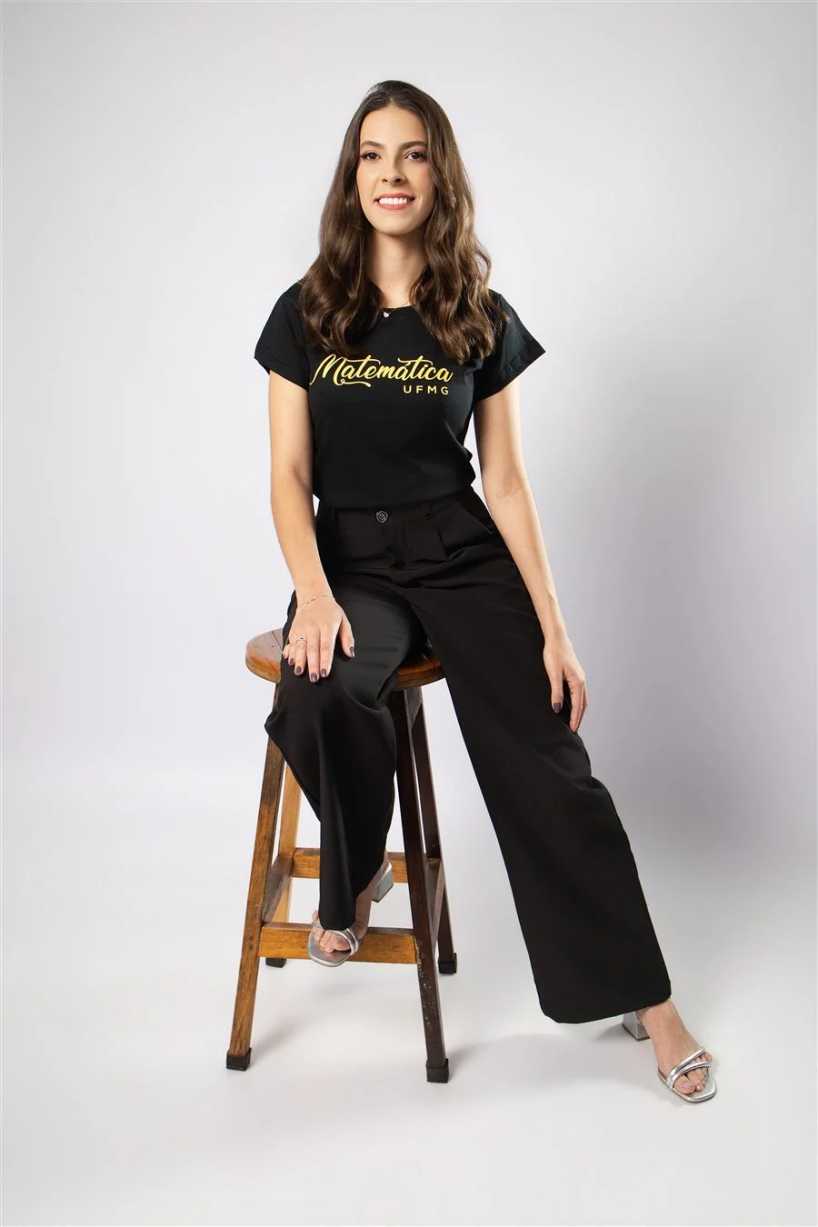 Formanda com camisa de Matemática sentada em banqueta alta de madeira