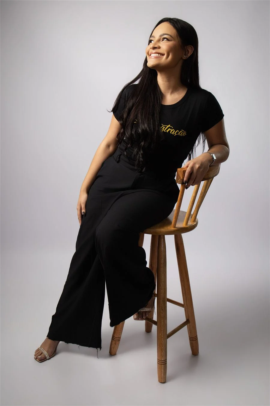 Formanda com camisa do curso sentada de lado em cadeira de madeira