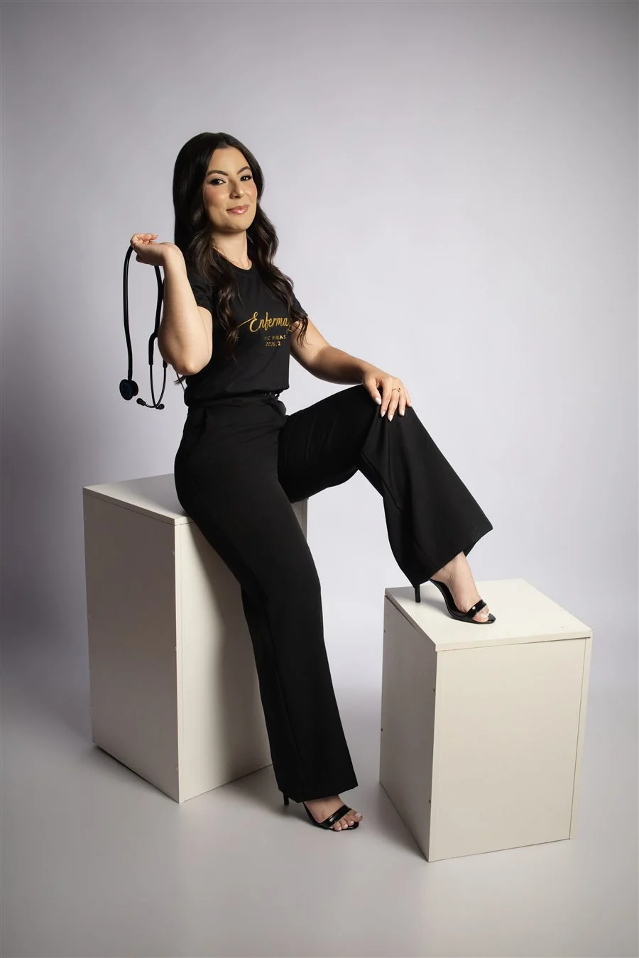 Formanda com camisa do curso sentada em cubo branco, com o pé apoiado em outro cubo