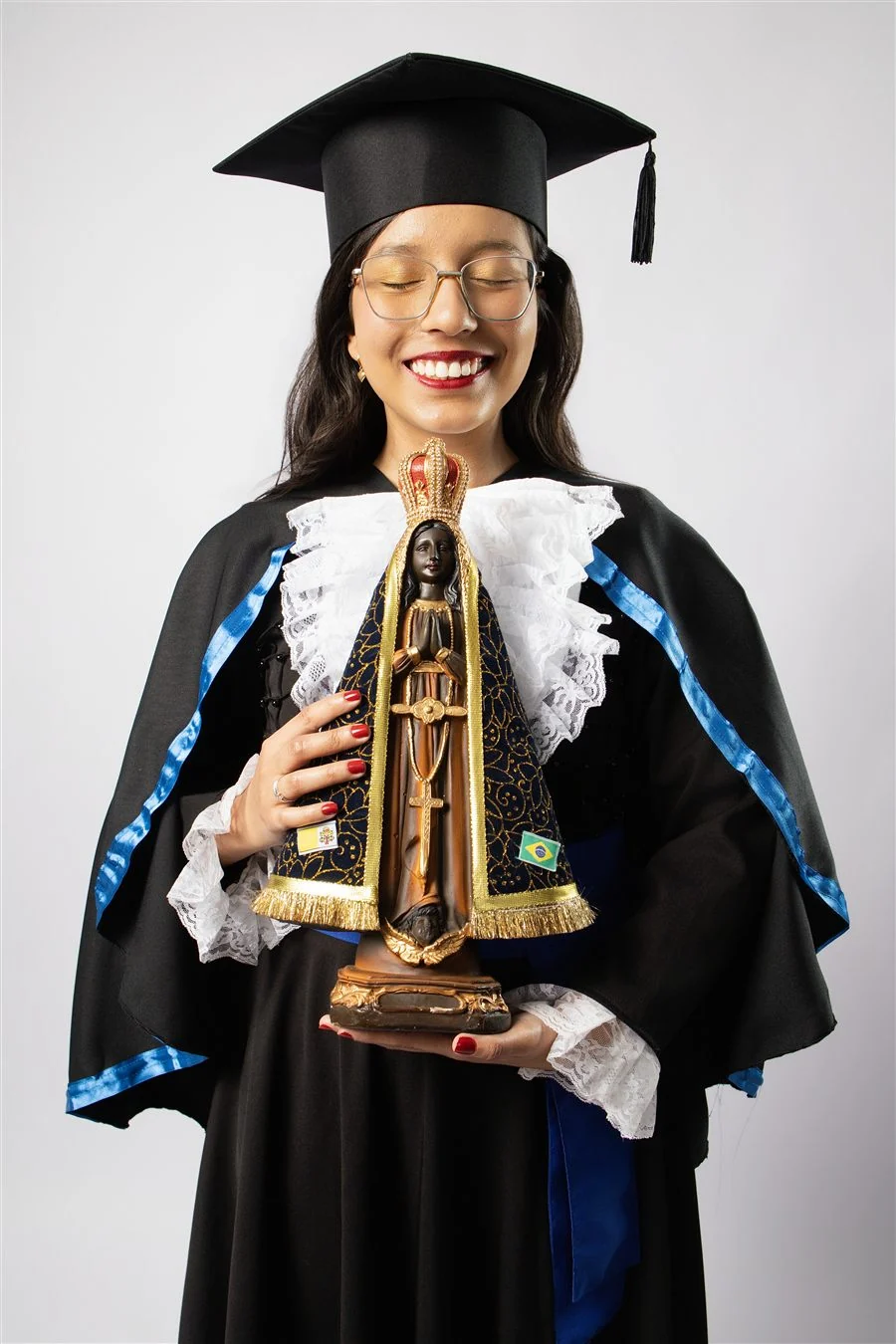Formanda de beca azul segurando uma imagem de Nossa Senhora Aparecida